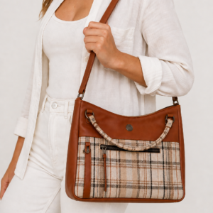 Woman wearing a handmade Molly tote bag in warm brown faux leather and neutral plaid fabric with a shoulder strap and exterior zipper pocket.