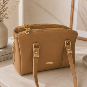 Neutral structured faux leather satchel handbag with gold hardware in a warm minimalist lifestyle setting.