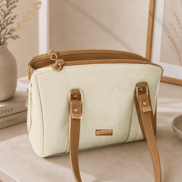 Neutral structured faux leather satchel handbag with gold hardware in a warm minimalist lifestyle setting.