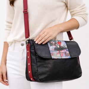black faux leather crossbody handbag with red strap worn on model