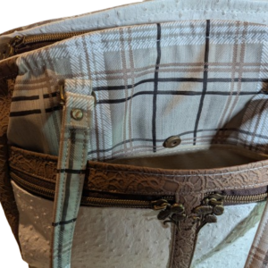 Front pocket detail on neutral handbag with plaid lining and zipper storage.