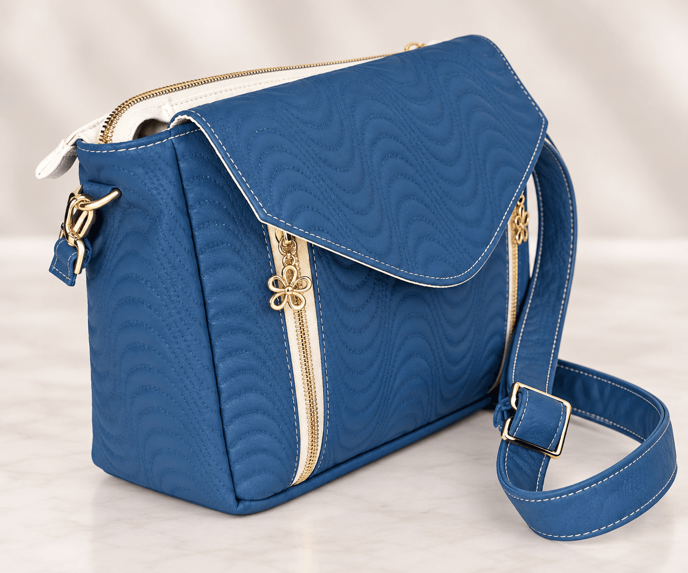 Angled view of blue quilted crossbody bag with gold zipper accents