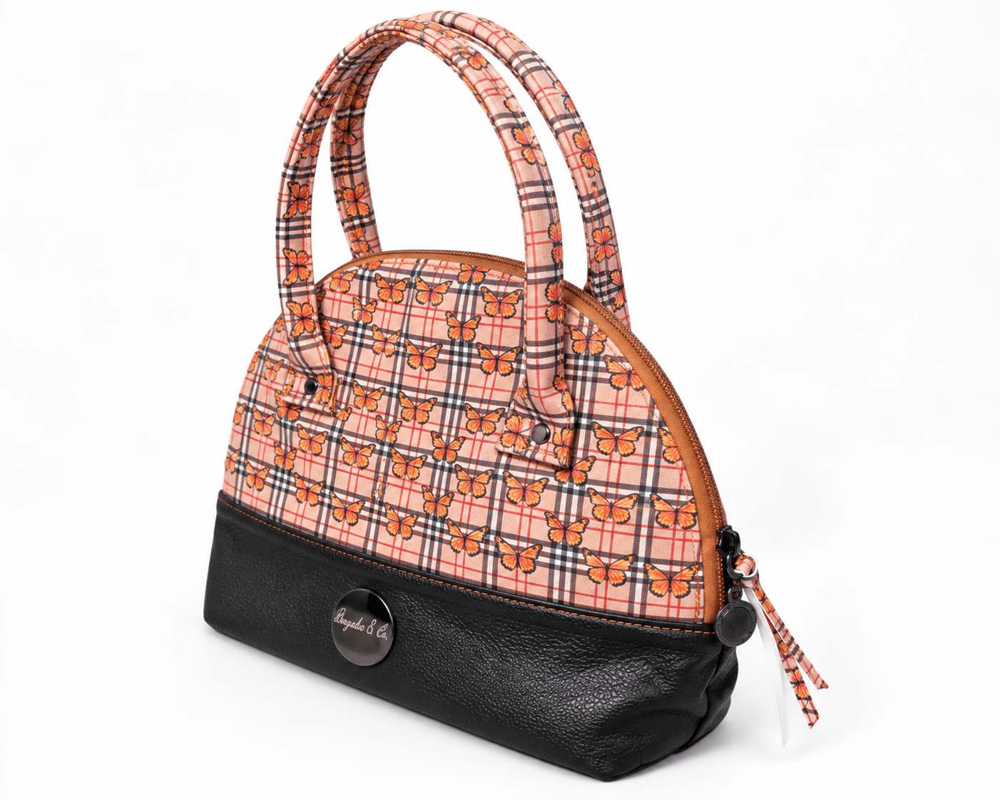 Angled view of orange butterfly plaid handbag showing its rounded shape, black faux leather base and top zipper closure.