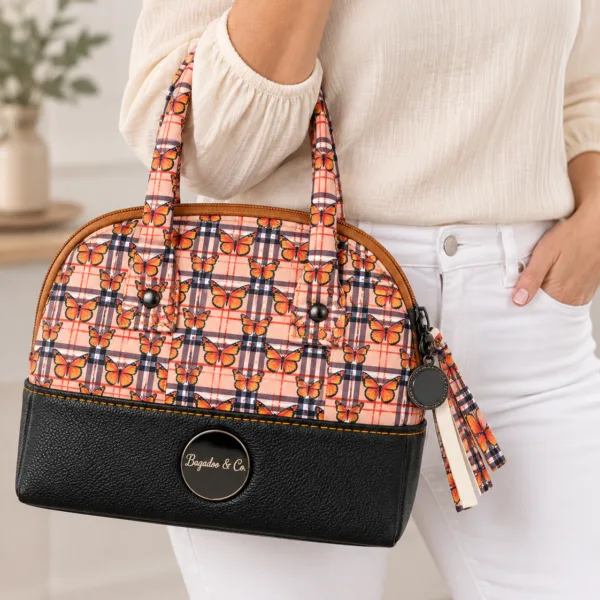 Model wearing an ivory blouse and white jeans carrying a compact orange butterfly plaid handbag with black faux leather base.
