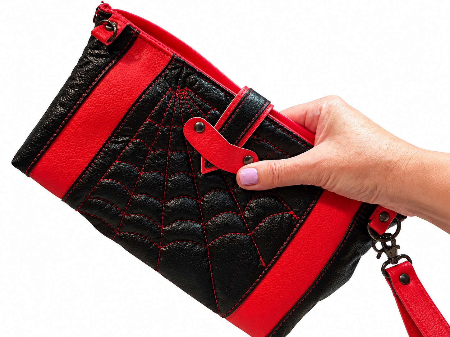 Red and black handmade wristlet held in one hand, showing raised spiderweb quilting, red faux leather accents, and detachable wrist strap.